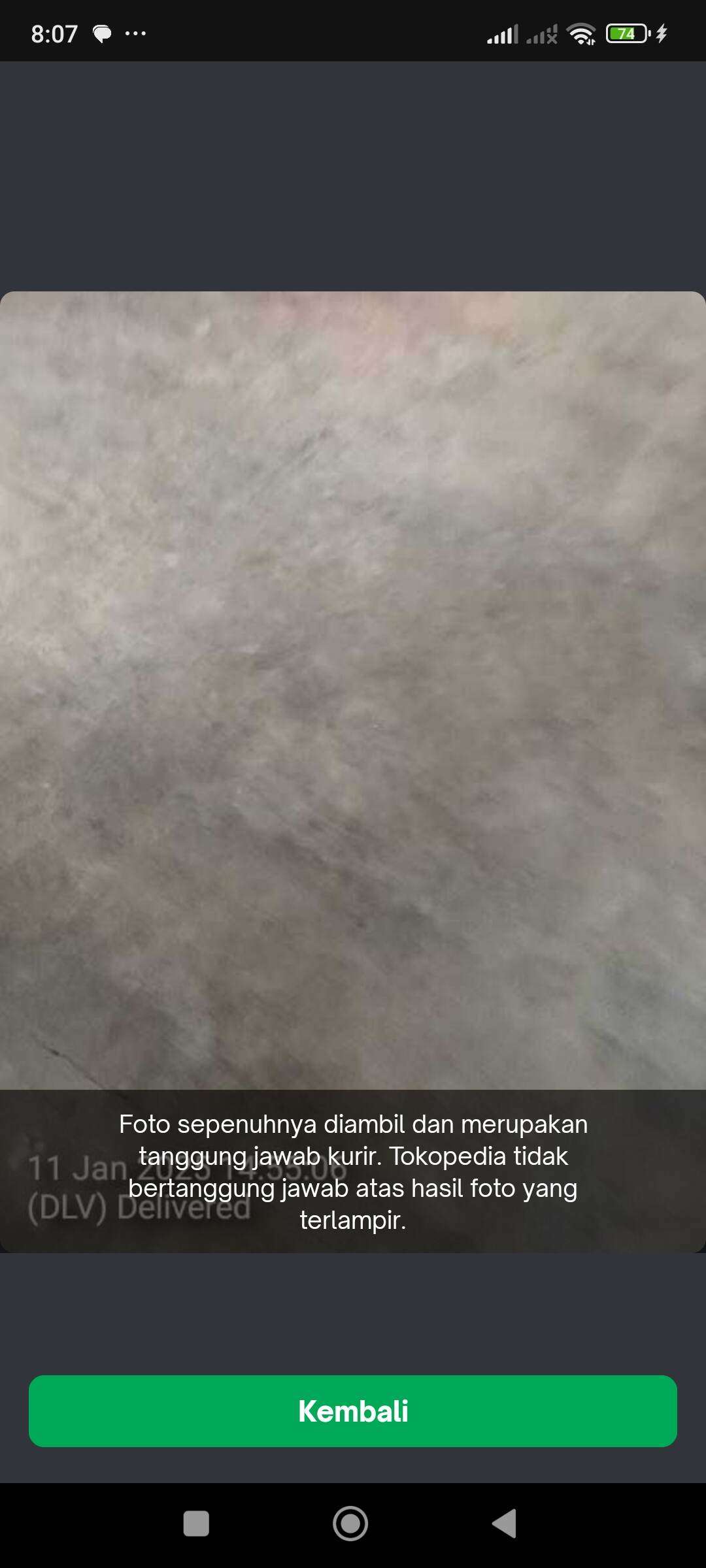 Foto bukti pengiriman yang tidak jelas, hanya menunjukkan gambar abu-abu yang tidak dapat dipastikan apakah itu plastik bubble wrap atau lantai marmer, tanpa menampilkan paket atau rumah saya.